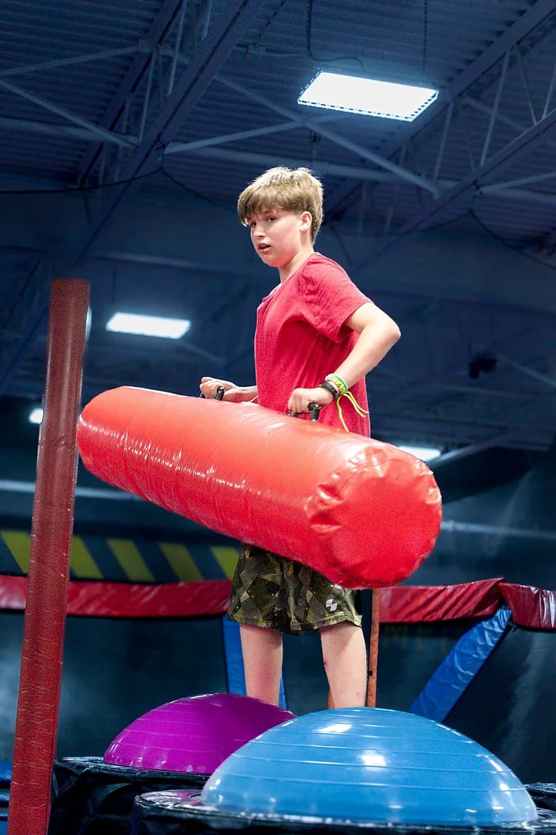 Kids playing on the Battle Beam attraction at AeroSports trampoline park