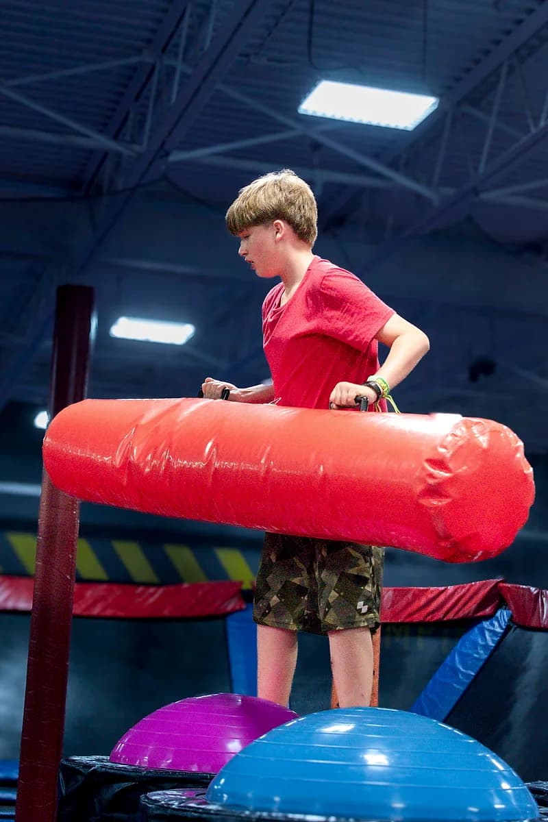 Kids playing on the Battle Beam attraction at AeroSports trampoline park